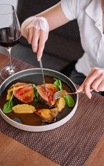 female hands holding a fork and knife and cuts roast duck with wine