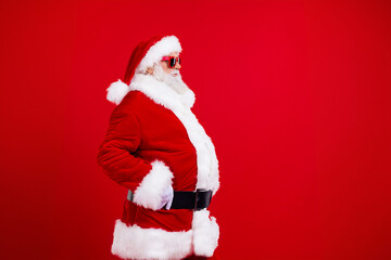 Fototapeta na wymiar Side profile photo of confident grandfather wear santa costume look at empty space hands on waist isolated on red color background
