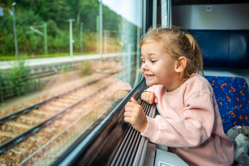 Happy little girl looking out train window outside, while it moving. Traveling by railway, Europe