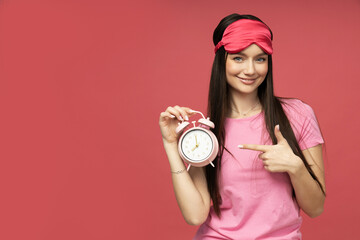 A young woman in a sleeping mask is holding an alarm clock