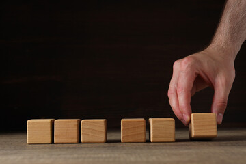Wooden cubes on wooden table and hand on black background, space for text