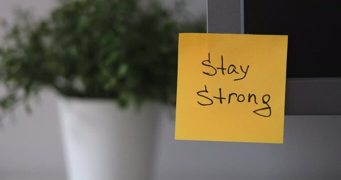A yellow paper notes with the reminder Stay Strong on it sticked on to a monitor at an office workplace.