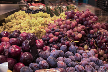 Grapes and plums on counter in supermarket, close up