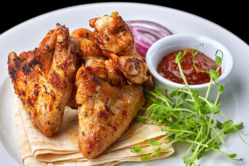 Grilled chicken wings with barbecue sauce, pita bread, microgreen and onion rings, on a white plate