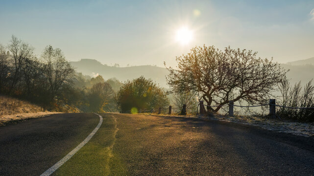 road through mountainous countryside in morning light. leafless tree on the hills. sun on the blue cloudless sky