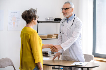 Smiling doctor shaking hands with mature woman patient at consultation