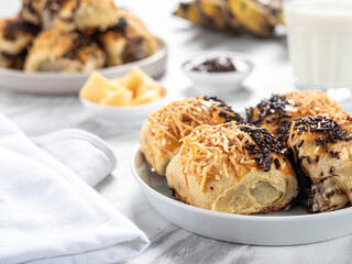 Bolen Pisang or Banana Wrapped is neatly presented on a white plate with decorations around it, isolated against a white and gray table background.