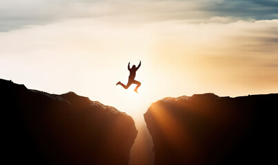 Man jumping over precipice between two rocky mountains at sunset. Freedom, risk, challenge, success - obrazy, fototapety, plakaty