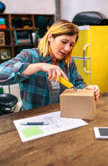 Blonde woman with cutter unpacking order received by courier with merchandise to sell on line....
