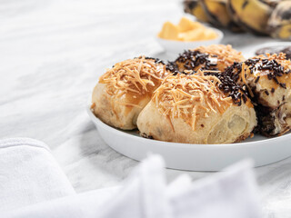 Bolen Pisang or Banana Wrapped is neatly presented on a white plate with decorations around it, isolated against a white and gray table background.