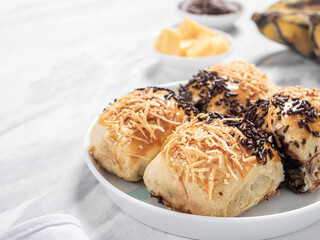 Bolen Pisang or Banana Wrapped is neatly presented on a white plate with decorations around it, isolated against a white and gray table background.