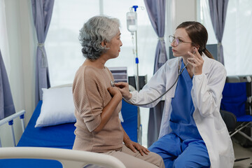 Young caretaker nurse uses stethoscope to check heartbeat. Elderly woman, cute cute nurse sitting in room on chair examining her patient and using her stethoscope, health care concept.
