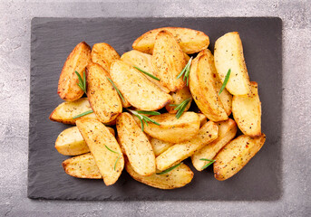 Baked potato wedges with seasonings on a stone tray on a gray st
