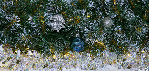 Christmas background with Christmas tree branches and silver tinsel in the light of golden garland