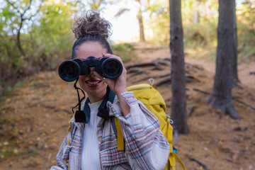 A curly-haired forest wanderer, enjoying the serene atmosphere of an autumn forest trail, accompanied by her trusty binoculars.