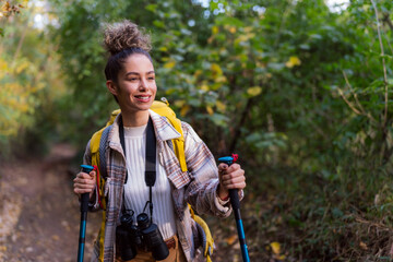 A curly-haired forest wanderer, enjoying the serene atmosphere of an autumn forest trail, accompanied by her trusty binoculars.