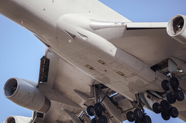 Close-up view of a cargo airplane's underside, taken from a low angle looking upwards. Landing plane. Detail pics. Blue sky.