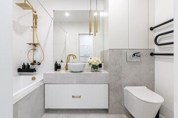 A modern bathroom in light colours with gold fixtures and a bouquet of white flowers