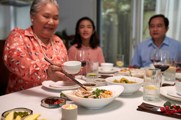 Grandmother taking some food from dish at family dinner table