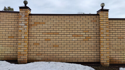 High stone modern fence made of yellow or white brick and columns with turrets. Background, texture, location © keleny