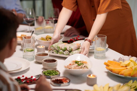 Woman Putting Plate With Spring Rolls On Dinner Table