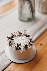 Top view of rustic style white cream cake decorated with fresh flowers, greens and happy birthday inscription on wooden table with natural linen tablecloth. Homemade dessert for birthday party