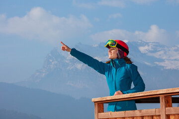 Smiling skier observes Alps from chalet, showing with finger