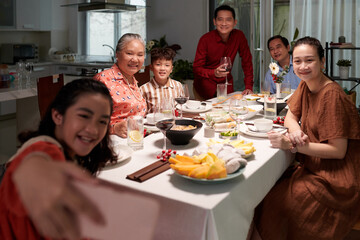 Smiling teenage girl taking selfie with her family at dinner table