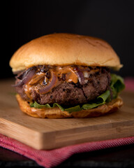 Juicy Homemade burger with lettuce onions, and chipotle sauce in a brioche bun. Dark and moody background.
