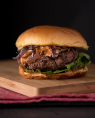 Juicy Homemade burger with lettuce onions, and chipotle sauce in a brioche bun. Dark and moody background.