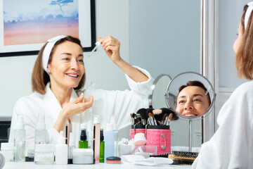 Happy woman putting facial serum with eyedropper on the face
