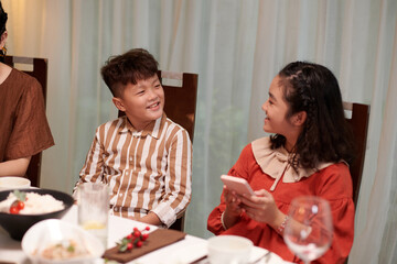 Smiling Vietnamese brother and sister taking at family dinner