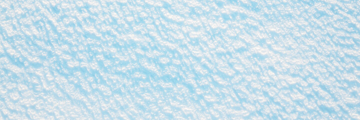 Wide panoramic winter background with snowy ground. Natural snow texture. Wind sculpted patterns on snow surface.