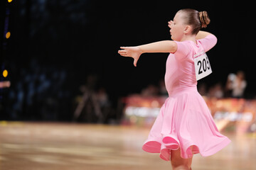Behind the dancer - a girl dancer-athlete in a pale pink dress against the background of the stage
