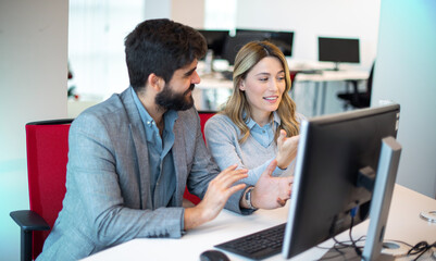 Two diverse businesspeople chatting sitting behind computer in office.Bearded businessman sharing ideas or startup business plan with female coworker.