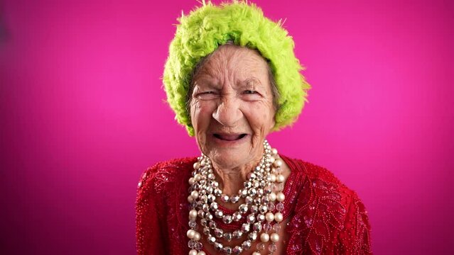 Displeased unhappy fisheye portrait caricature of funny elderly woman saying NO with green hat isolated on pink background.