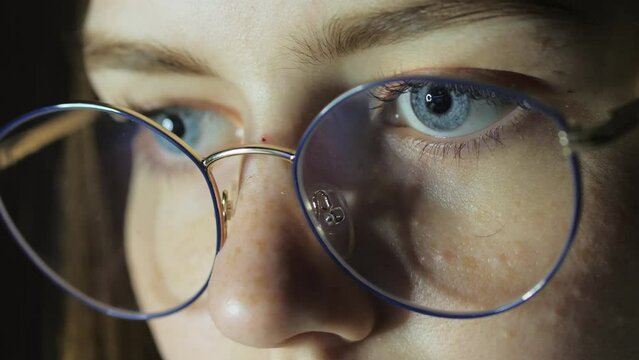 Close-up eyes of a teenage girl with glasses looks at the monitor, plays a game, reads, studies late at night