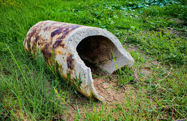 An abandoned broken cement pipe lies on the grass.