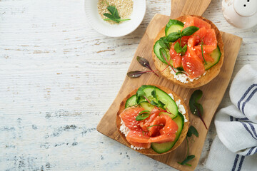 Open smoked salmon sandwiches with cream cheese, cucumber, sesame seeds, microgreens, spinach, and peas leaves on light old wooden background. Healthy breakfast food. Delicious snack. Top view.