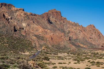 A road, cutting through a mountinous, volcanic landscape. The location in Mount Teidi, on Tenerife. It is the highest point in Spain. 