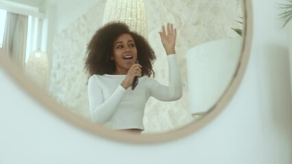 Pretty funny expressive curly young woman with smartphone looking at mirror reflection dancing and singing at home Cute female enjoying free time in light room in morning before work or study indoors