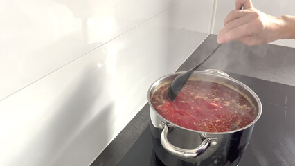 Women's hands stir a ladle in a pot of red soup, in the home kitchen. The process of cooking...