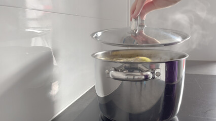 Women's hands open the lid of a pot of boiling soup in a home kitchen. The process of cooking...