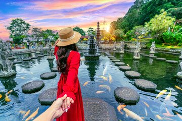 Women tourists holding man's hand and leading him to Tirta Gangga Water Palace in Bali, Indonesia.