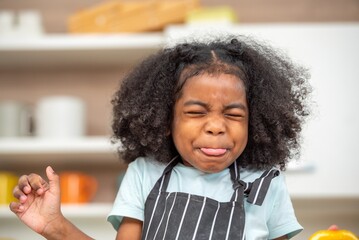 african afro hair black kid Cute taste oranges citrus sour flavour on ripe mouth in kitchen. candid...