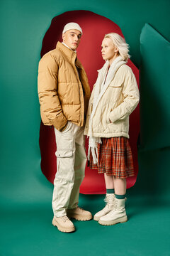 full length of couple in modern winter jackets posing together on red with turquoise backdrop