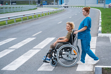 Red-haired nurse pushing an elderly woman in a wheelchair across the road. 