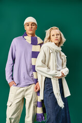 couple in winter outfits, blonde woman posing with man in trendy clothing on turquoise backdrop