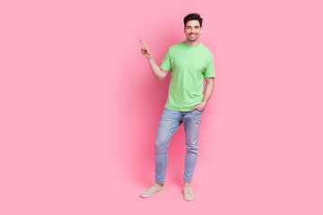 Full length photo smiling man wear green stylish t shirt and jeans indicate finger mockup tv media advert isolated on pink color background