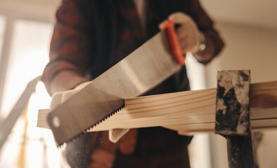Construction worker cutting wood with a crosscut saw to renovate a home - obrazy, fototapety, plakaty